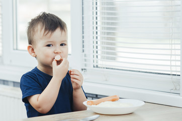 baby eating sausage in the kitchen is very charming and emotional