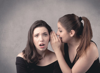 Two fancy dressed actress girls with long hair and make up whispering in front of grey urban background concept.