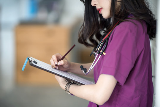 Nurse in purple uniform standing at patient room and writing on medical chart - Powered by Adobe