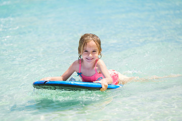 Little baby girl - young surfer with bodyboard has a fun on small ocean waves. Active family lifestyle