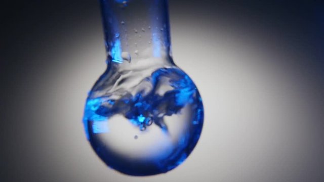 An impressive macro shot of clean water in a round bottom flask rotated in a chemical lab. The water plays with blue and grey shadows.