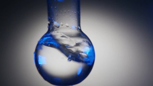 An exciting macro shot of clean water in a round bottom flask shaken in a chemical lab. The water plays with blue and grey tints.
