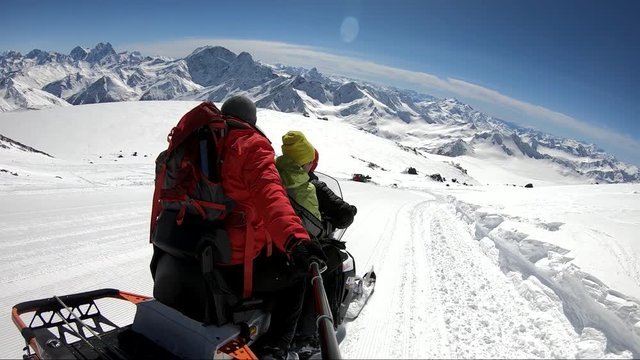 Snowmobile with tourists descends on a snowy slope high in the mountains