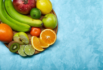 Ripe fresh fruits in a wooden plate on a blue background, selective focus, close-up, top view