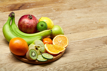 Ripe fresh fruits in a wooden plate on a light wooden background, selective focus, close-up, top view
