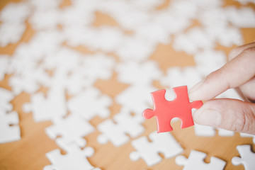 Hand holding red piece of blank jigsaw puzzle with wooden table background.