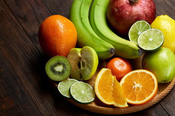 Ripe fresh fruits in a wooden plate on a rustic wooden background, selective focus, close-up, top view