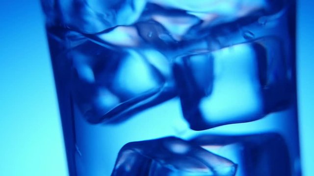 A stylish macro shot of five ice cubes shaken in a glass with water covered with splashes  in studio. They are just dancing elegantly
