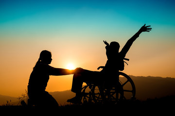 Happy boy in wheelchair and sister on sunset. Happy disabled child concept