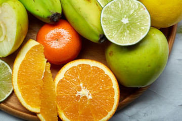 Ripe fresh fruits in a wooden plate on a light background, selective focus, close-up, top view