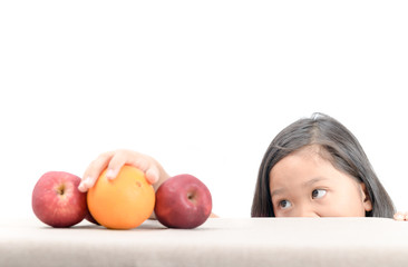 Cute asian girl is reaching orange on table