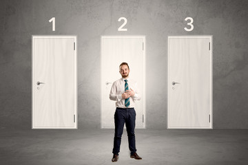 Fototapeta premium Businessman in grey room with three numbered white door behind his back 