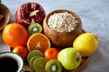 Bowl with oatmeal flakes served with fruits on wooden tray over rustic background, flat lay, selective focus