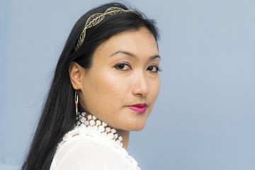 Close-up portrait of an attractive Thai woman. Outdoor portrait of an Asian Thai woman in white dress, blue wall in background.