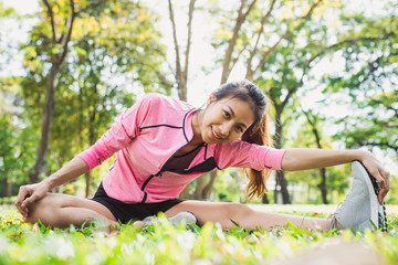 Naklejka na ściany i meble Healthy young asian woman exercising at park. Fit young woman doing training workout in morning. Young happy asian woman stretching at the park after a running workout. Exercise outdoor concept.