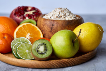 Bowl with oatmeal flakes served with fruits on wooden tray over rustic background, flat lay, selective focus