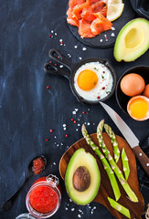 Top view of breakfast table with fried eggs, avocado, asparagus, red caviar and smoked salmon, copy space