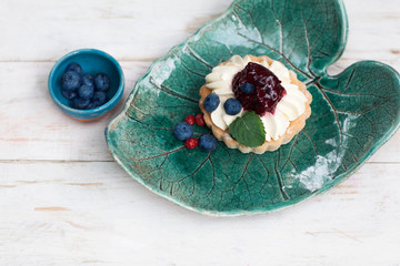 art with berry cream and blueberries on a ceramic green plate on white wooden background
