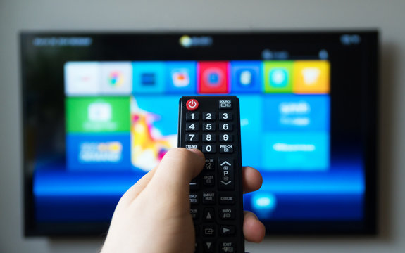 Male hand holding TV remote control. Smart TV.