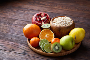 Bowl with oatmeal flakes served with fruits on wooden tray over rustic background, flat lay, selective focus