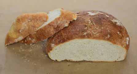 Closeup of half a loaf of fresh home bread and cut from it hunch of bread on parchment for baking , crumbs of fresh bread