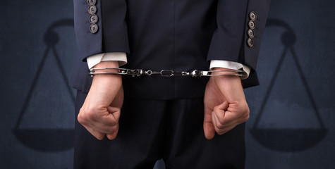 Arrested businessman in handcuffs with hands behind back and justice symbol wallpaper
