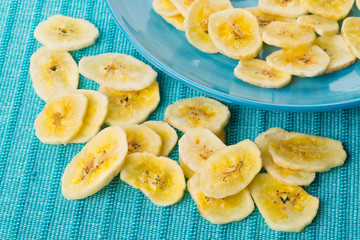 Heap of dried banana chips snack on blue turquoise plate and mat