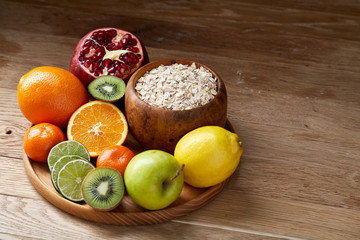Bowl with oatmeal flakes served with fruits on wooden tray over rustic background, flat lay, selective focus