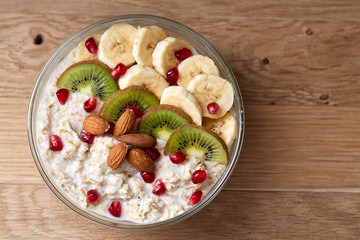 Delicious oatmeal porrige with fruits in glass bowl over rustic wooden background, shallow depth of field, close-up.