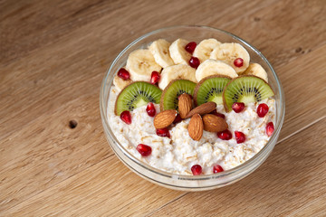 Delicious oatmeal porrige with fruits in glass bowl over rustic wooden background, shallow depth of field, close-up.