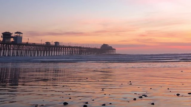 California Oceanside pier at sunset with reflections on wet beach sand