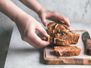 Butter-free,sugar-free banana bread with oat flour,soft curd cheese,honey. Woman hand with slice of banana bread on gray table. Ideas recipe healthy diet breakfast. Selective focus