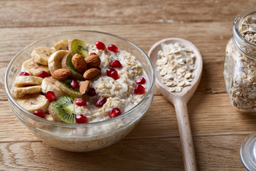 Delicious oatmeal porrige with fruits in glass bowl over rustic wooden background, shallow depth of field, close-up.