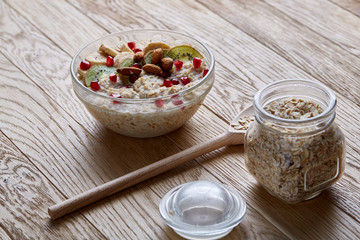 Delicious oatmeal porrige with fruits in glass bowl over rustic wooden background, shallow depth of field, close-up.