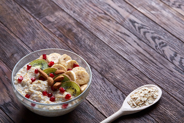 Diet breakfast oatmeal with fruits, bowl and spoon with oat flakes, selective focus, close-up