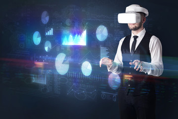 Elegant businessman in DJI goggles handling 3D reports and charts around him
