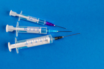Medical syringes of different capacities lie on a blue surface.