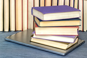 On the table are a number of books and a gray laptop under a pile of books.