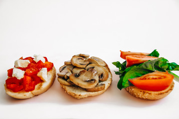 Vegetarian food on white isolated background. Italian bruschetta three kinds: tomatoes with spinach, feta cheese and sweet pepper, fried champignons. Side view