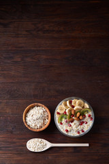 Fototapeta na wymiar Bowl with oatmeal flakes served with fruits on wooden tray over rustic background, flat lay, selective focus