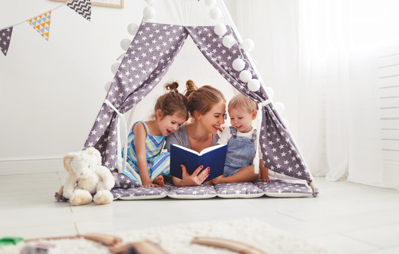 family mother reading to children book in tent at home.