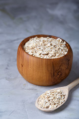 Oat flakes in bowl and wooden spoon isolated on wooden background, close-up, top view, selective focus.