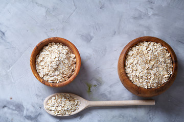 Oat flakes in bowl and wooden spoon isolated on wooden background, close-up, top view, selective focus.