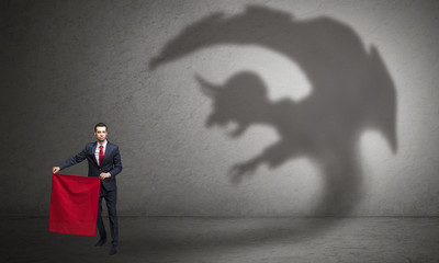 Businessman standing with red cloth in his hand and imp shadow on the background

