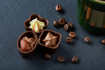 Coffee cup, coffee beans, chocolate candies on stone board over wooden background, selective focus, close-up