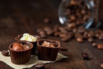 Side view of overturned glass jar with coffee beans and chocolate candies on wooden background, selective focus