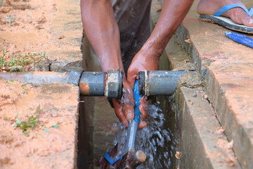 A worker repairing galvanized iron pipes without any safety equipment like helmet or boots.