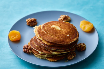 Pile of homemade pancakes with walnuts on blueish plate over blue background, selective focus
