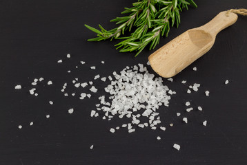 Salt heap on black background with rosemary herb and wooden spoon © Madele
