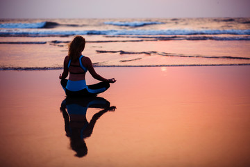 Woman practicing yoga on the beach at sunset